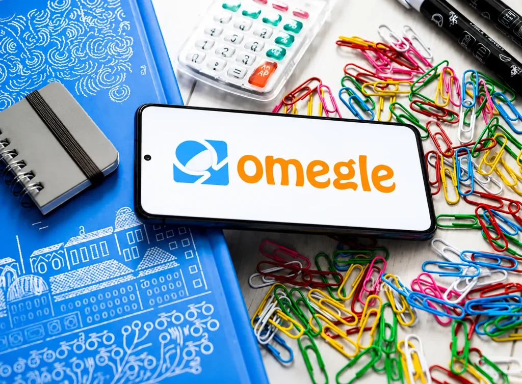 Omegle replacement logo displayed on a smartphone surrounded by colorful paperclips, notebook and desk supplies
